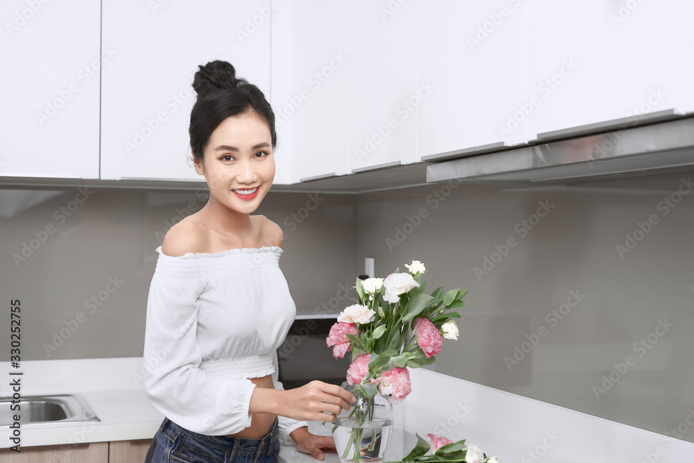 Young Asian woman taking flowers in kitchen.