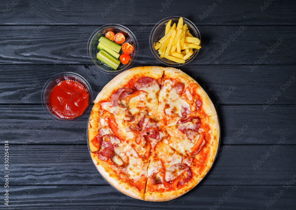 Fresh hot pizza with with french fries and vegetables on a dark background