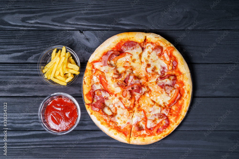 Fresh hot pizza with french fries on a black surface. Fast food concept.