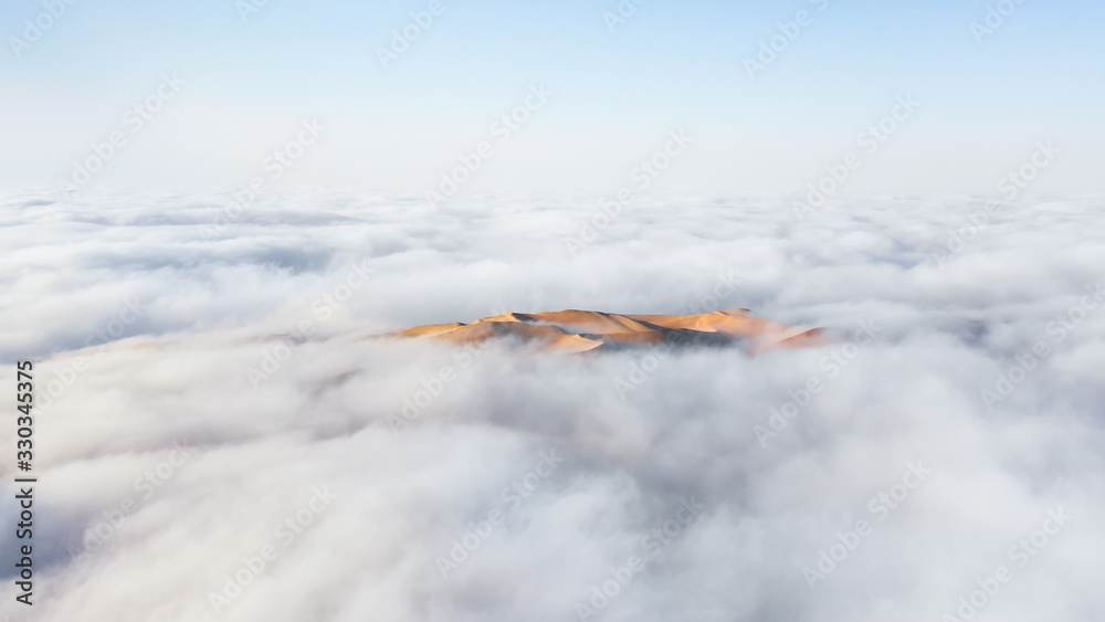 Aerial view of a massive sand dune surrounded by winter morning fog cloud in Empty Quarter. Liwa des