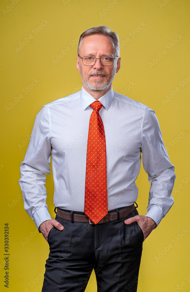 Portrait of a senior man smiling. Man looking at camera. Business man in studio, yellow backgroung. 