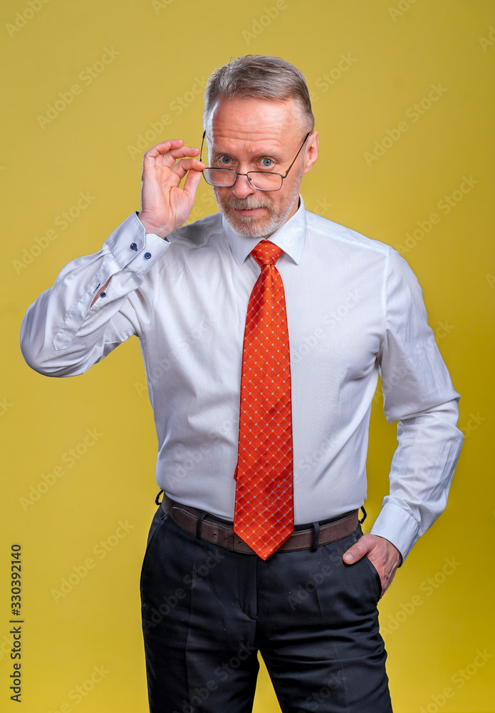 Portrait of a senior man in glasses. Man looking at camera. Business man in studio, yellow backgroun