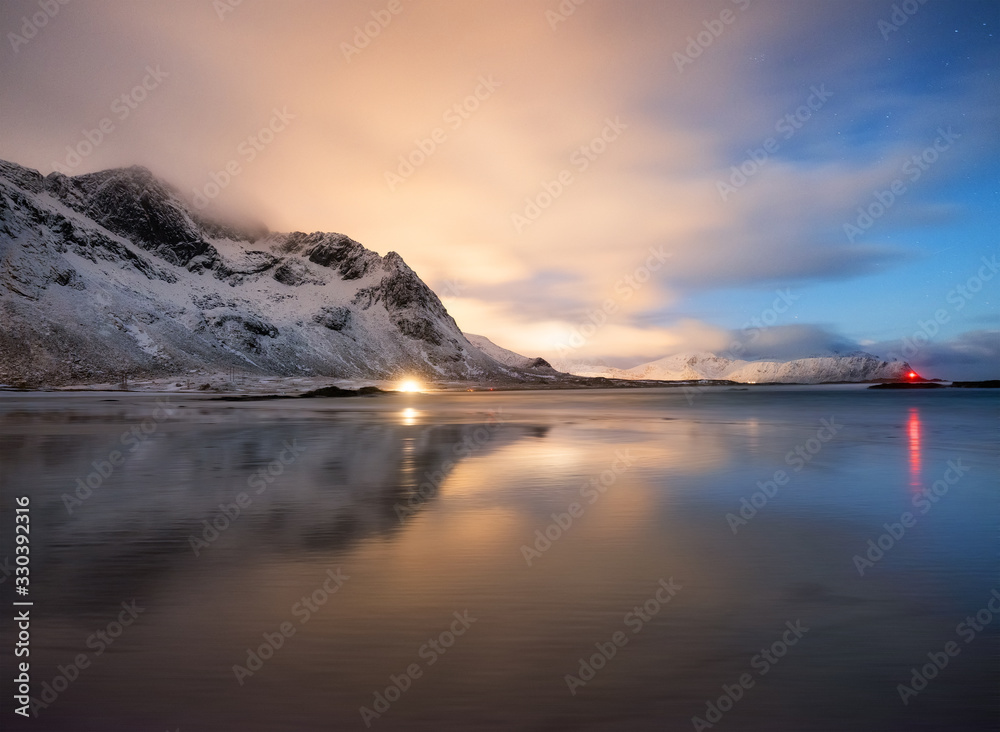 Mountains and reflections on beach at night. Winter landscape. The sky with stars and clouds in moti