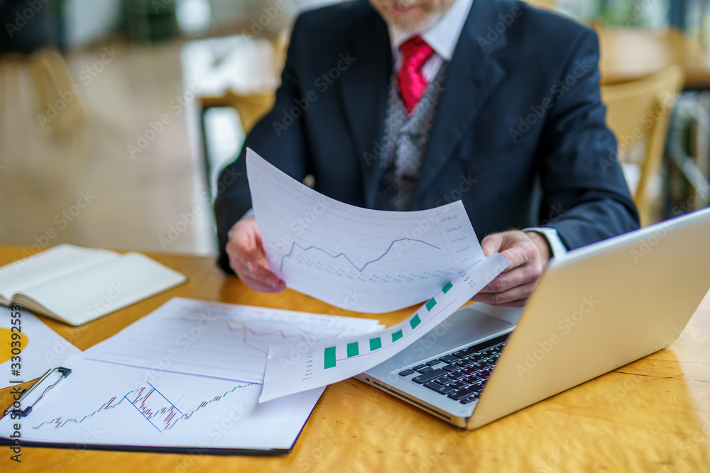 Businessman is reading a printed report or document. Man sitting at the table, working on paper work