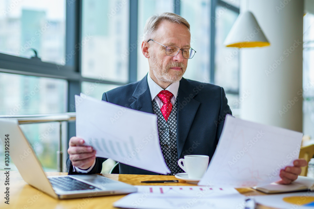 Thoughtful businessman is reading important business papers. Photo in front of the window with city 