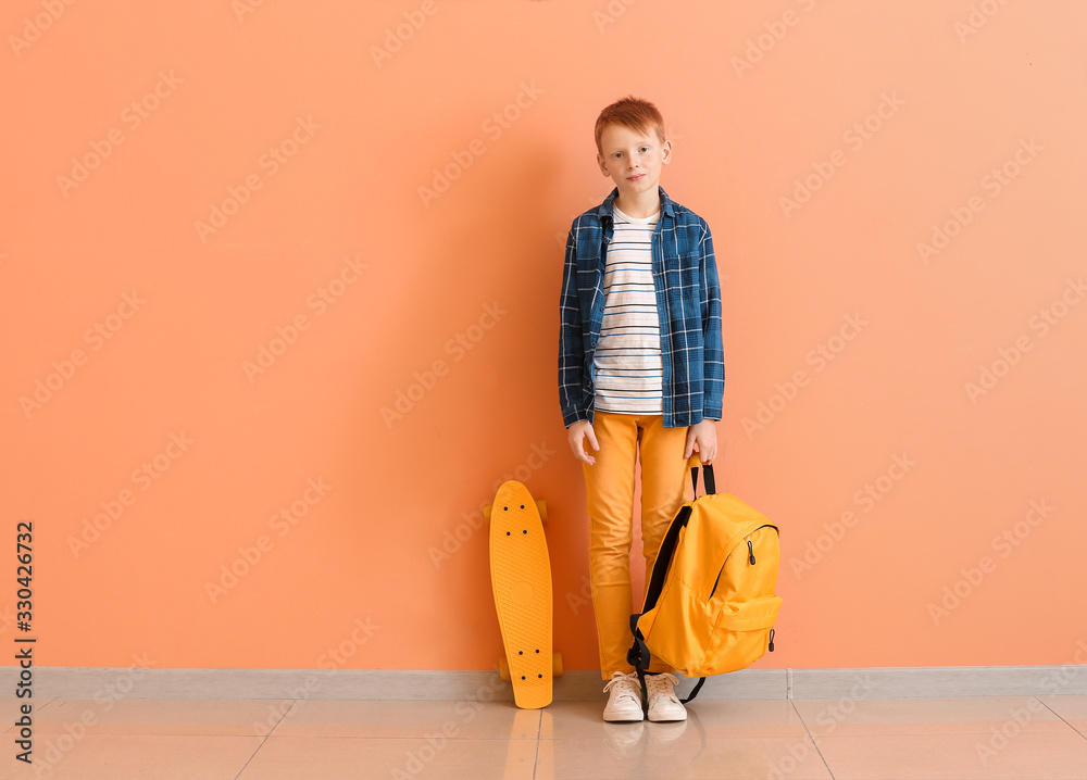 Cute little boy with skate and backpack near color wall