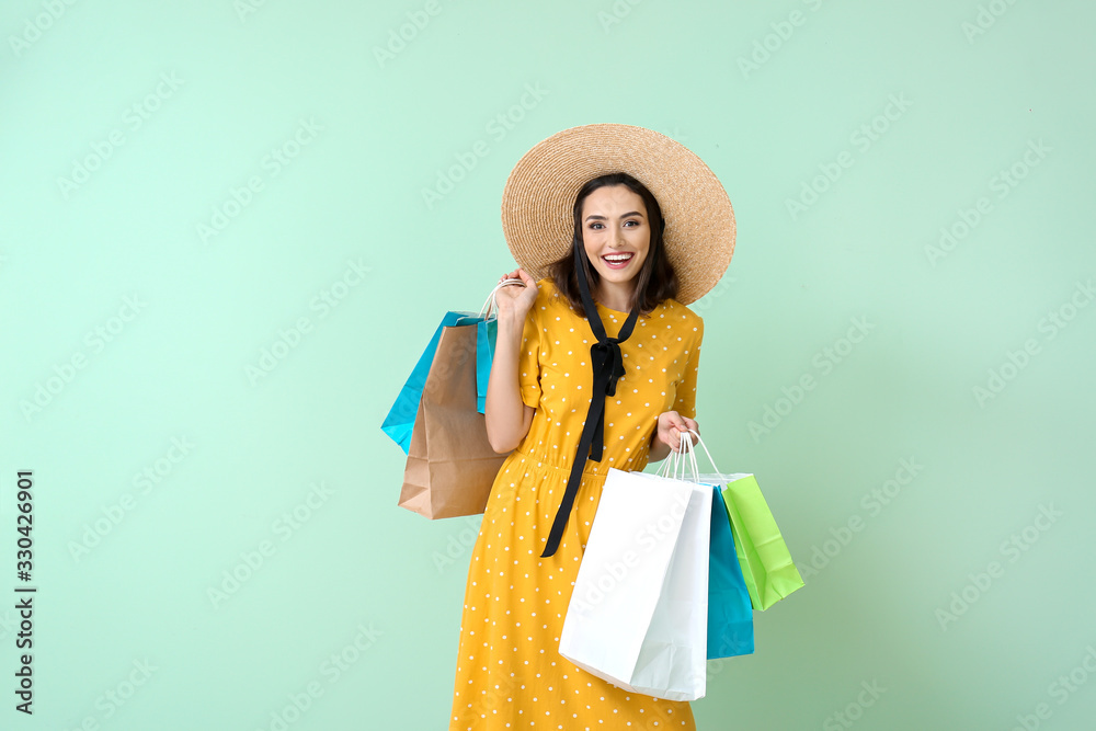 Beautiful young woman with shopping bags on color background