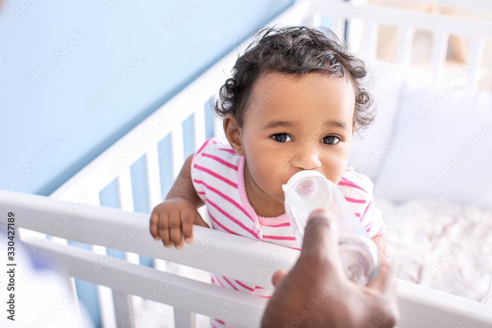 African-American man giving water to his cute baby at home