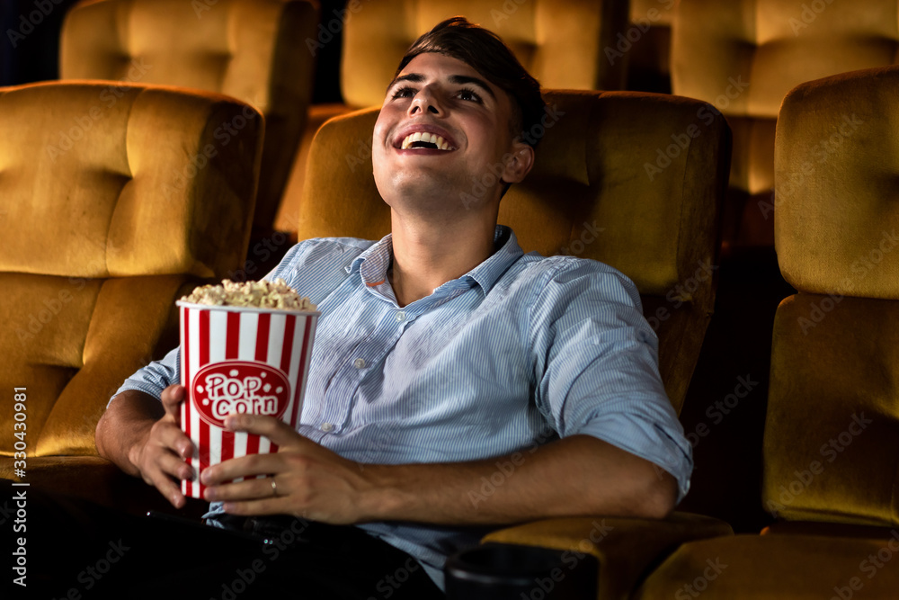 A young man smiling enjoying with his popcorn while watching a movie in theater cinema