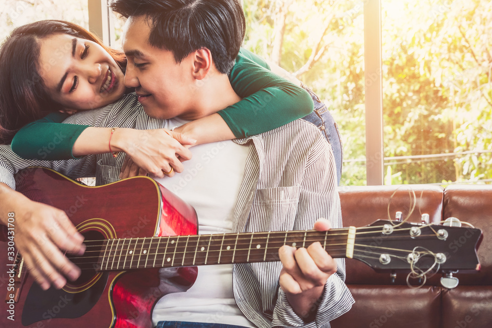 Young Asian Couple Plays Guitar and Sing Song in Living Room at Home Together. Music and Lifestyle c