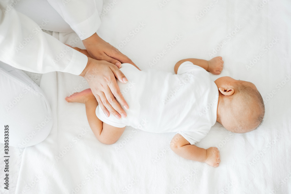 Young Asian mother touching her newborn baby with love on white bed, mothers day concept