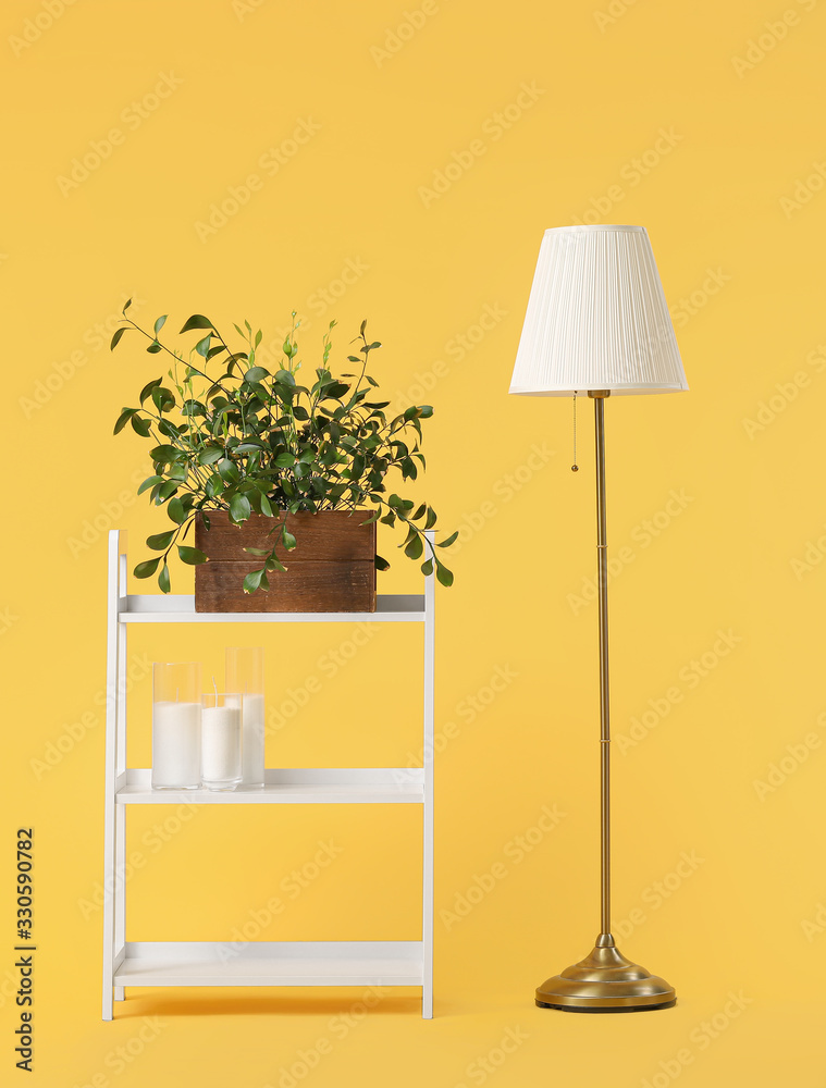 Shelving unit with decor and lamp on color background