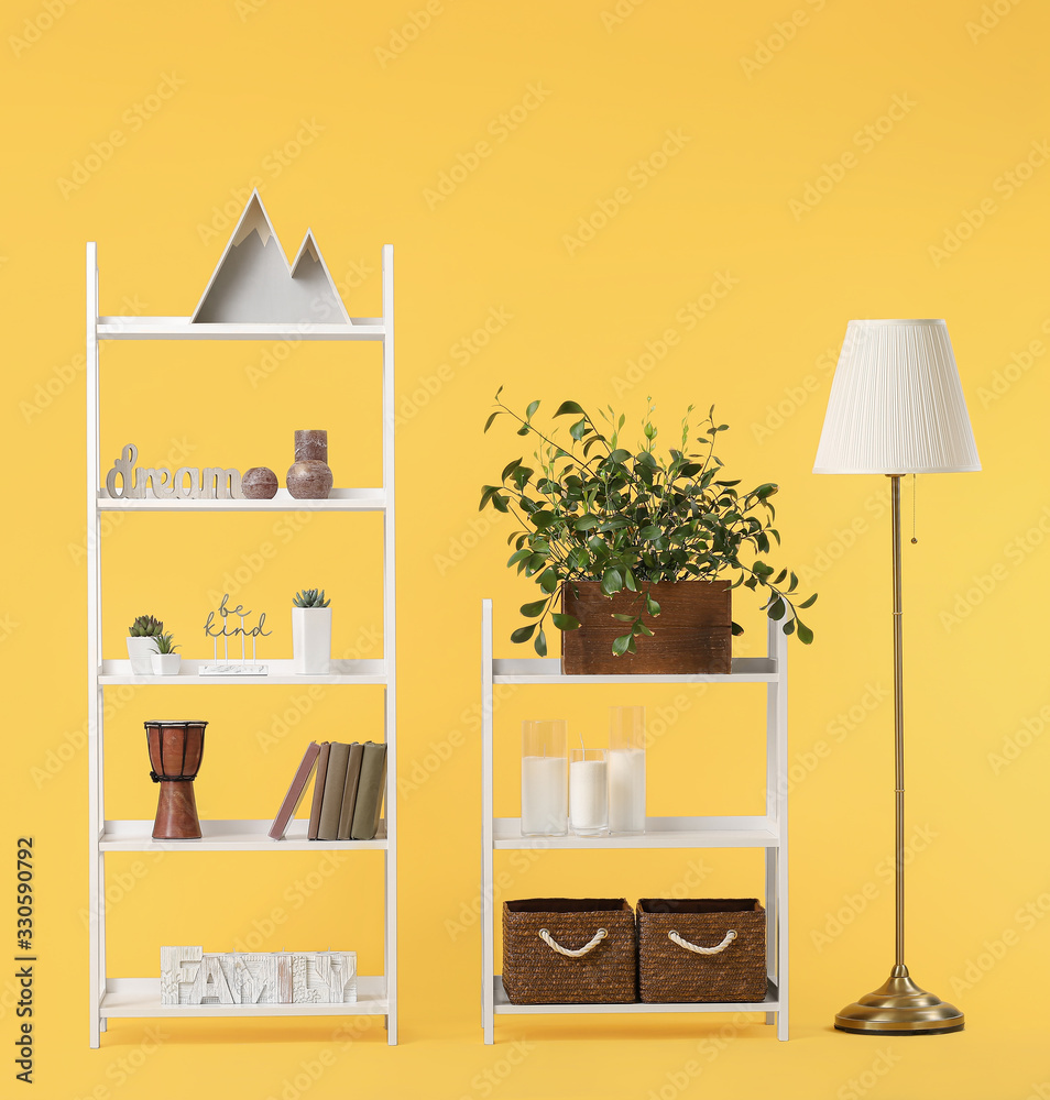 Shelving units with decor and lamp on color background