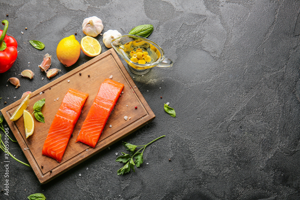 Raw salmon fillet with vegetables, oil and lemon on dark background