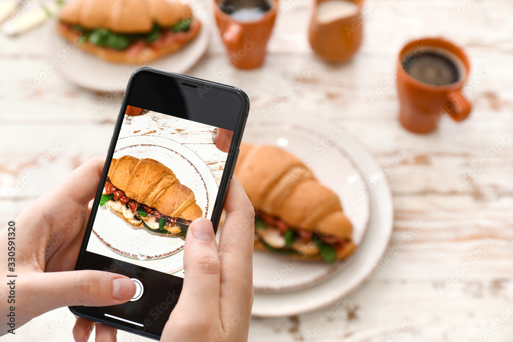 Woman taking photo of tasty croissant sandwich on table