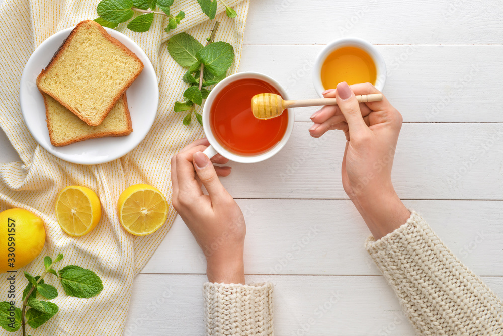 Woman drinking tea with honey at table, top view