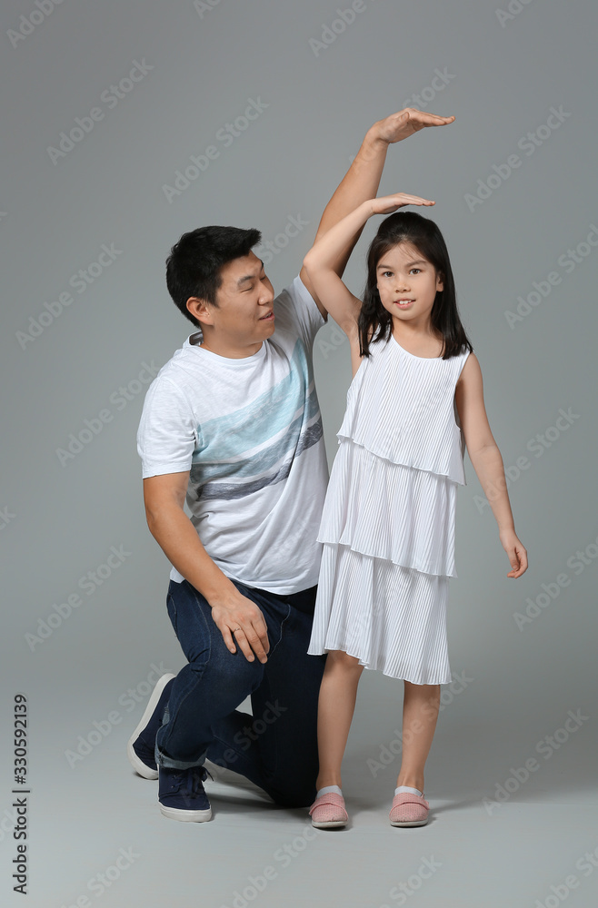 Happy Asian man and his little daughter measuring height on grey background