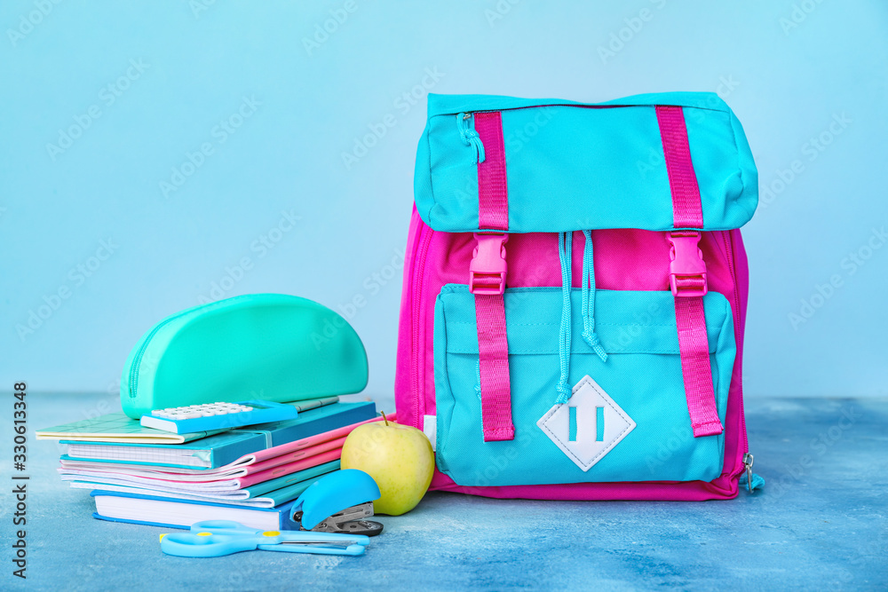 School backpack and stationery on color background