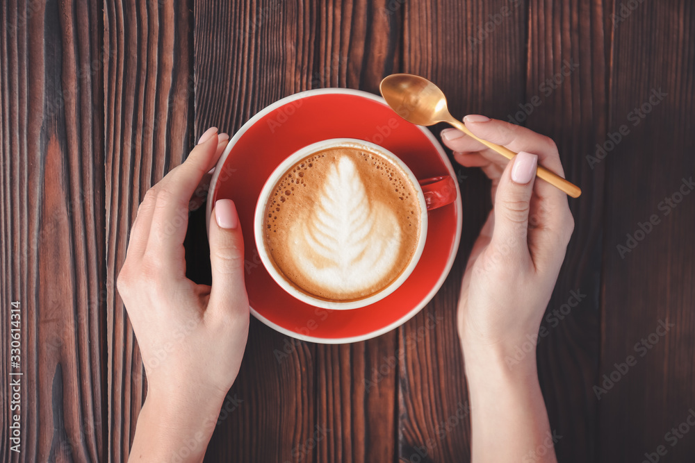 Woman drinking tasty cappuccino at wooden table