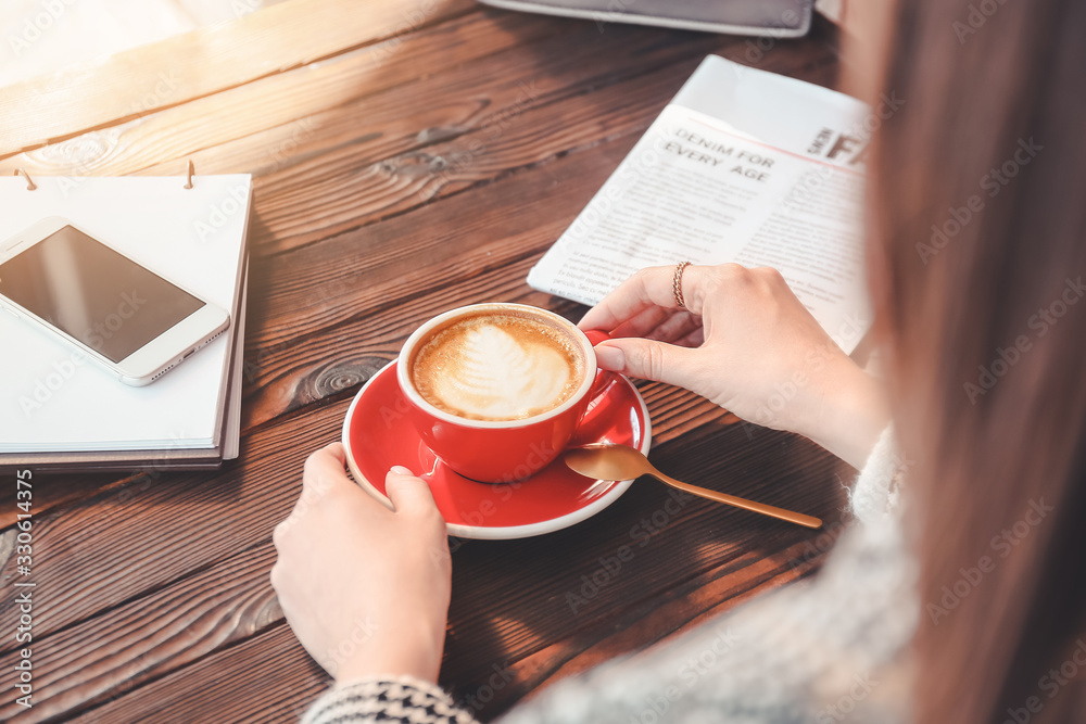 Woman drinking tasty cappuccino at wooden table