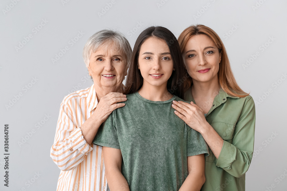 Portrait of mature woman with her adult daughter and mother on grey background