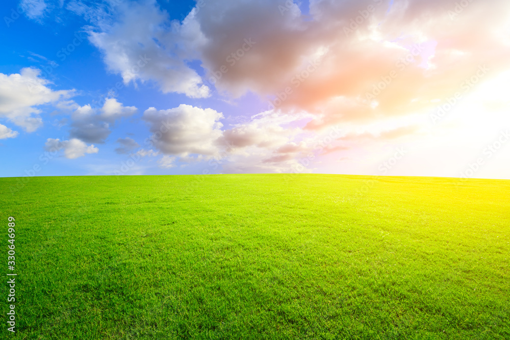 Green grass field and colorful sky clouds at sunset.