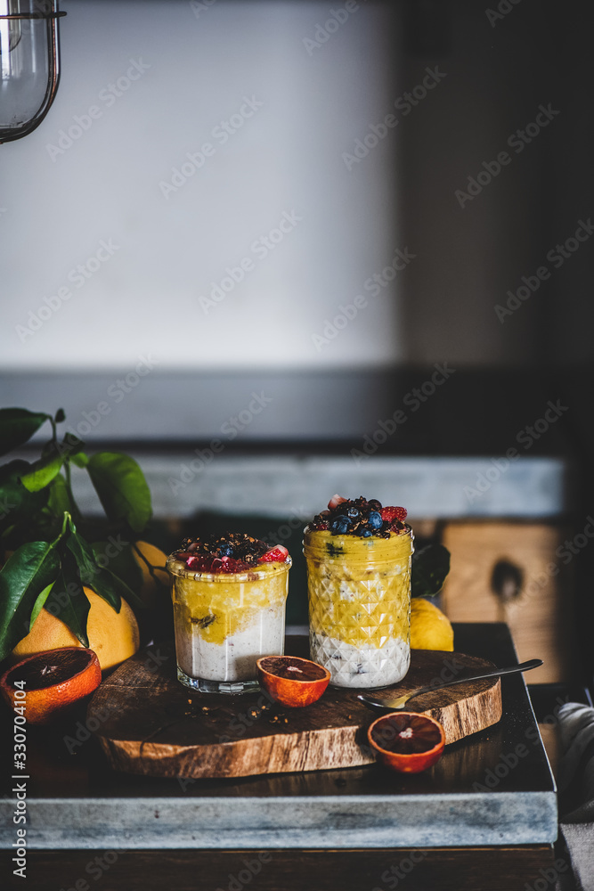 Overnight oat bircher muesli with mango smoothie, buckwheat granola and fresh berries in glasses ove