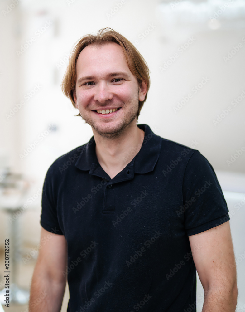 Portrait of a confident male doctor. Man in black shirt standing at blurred medical office backgroun