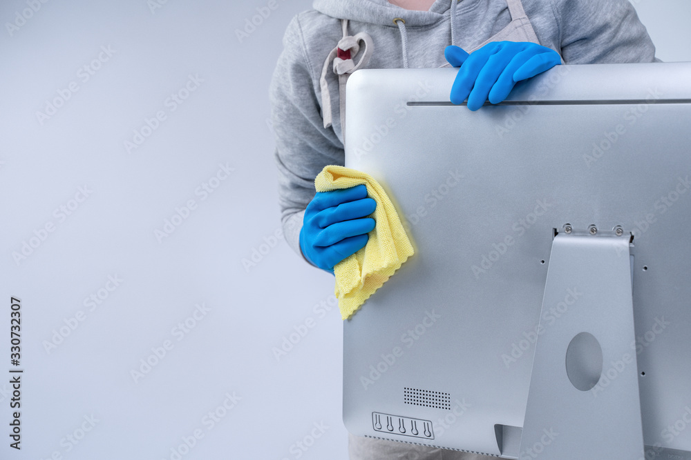 Young woman housekeeper in apron is doing cleaning silver computer screen with blue gloves, wet yell