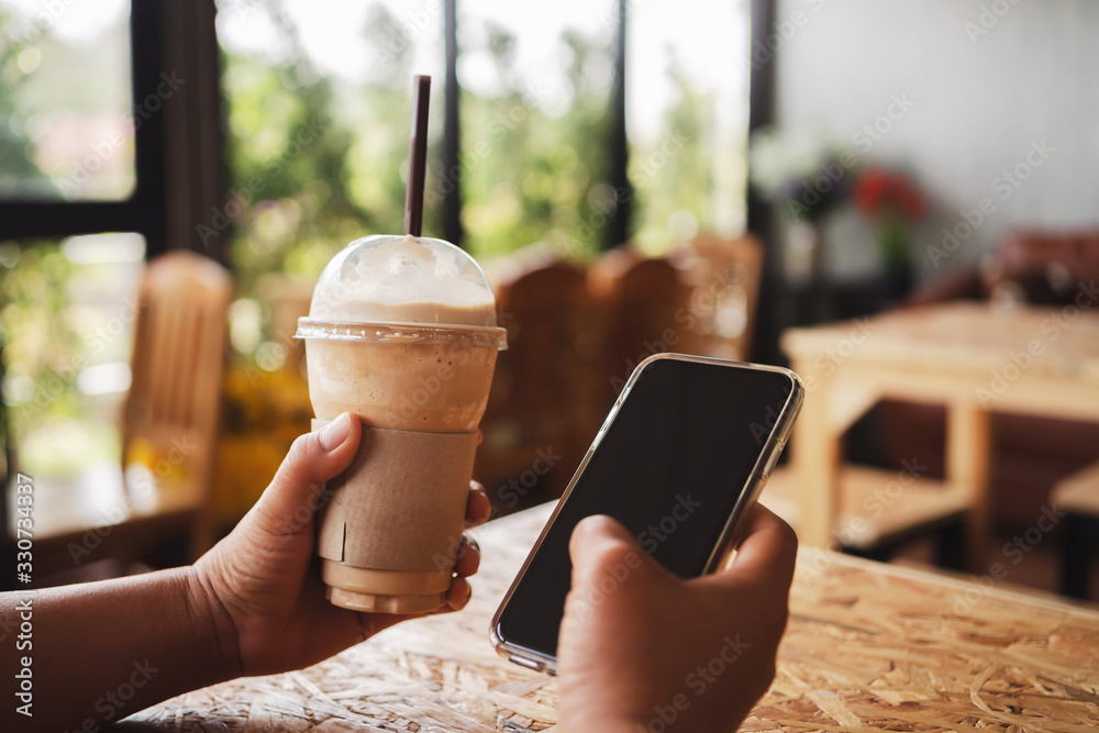 woman hand holding coffee in plastic cup and mobile phone in shop