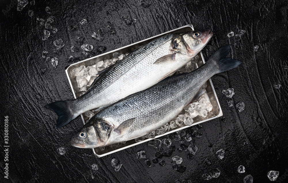 Seabass fish on metal tray on black stone background