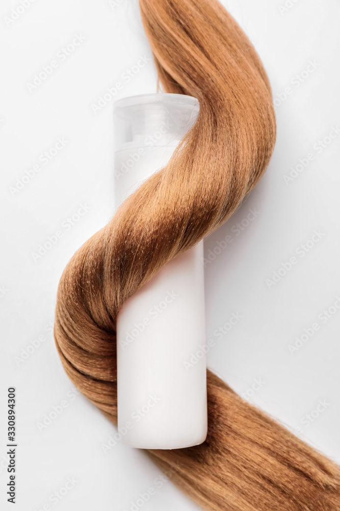 Bottle of shampoo and hair strand on white background