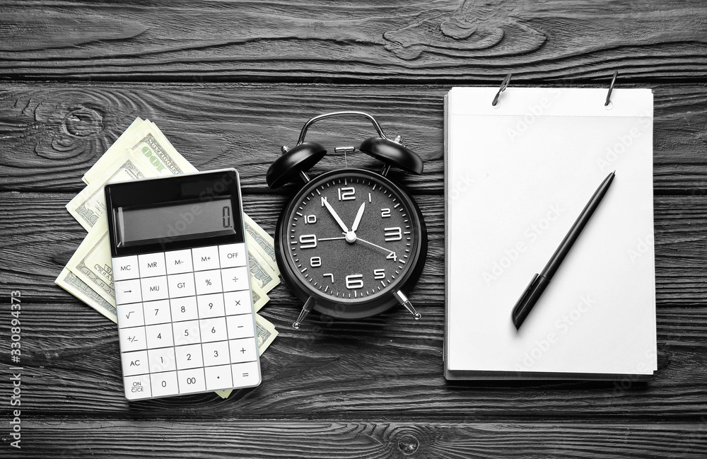 Alarm clock with notebook, calculator and dollar banknotes on dark wooden background. Time managemen