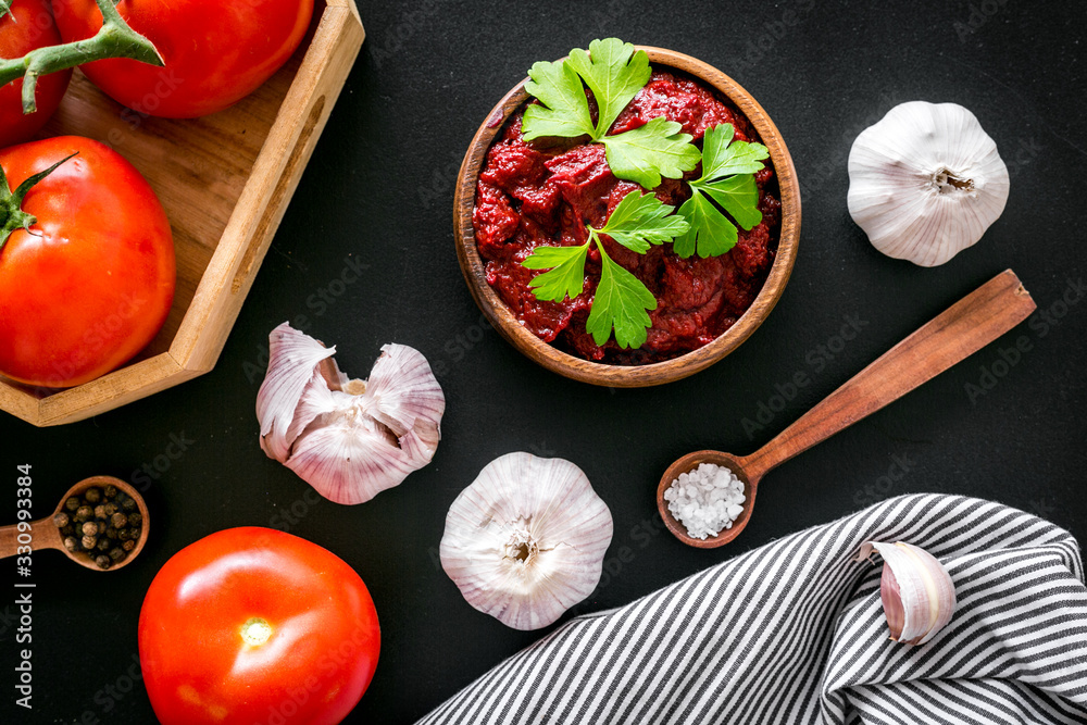 Homemade tomato sause near ingredients - garlic, spices - on black background top-down