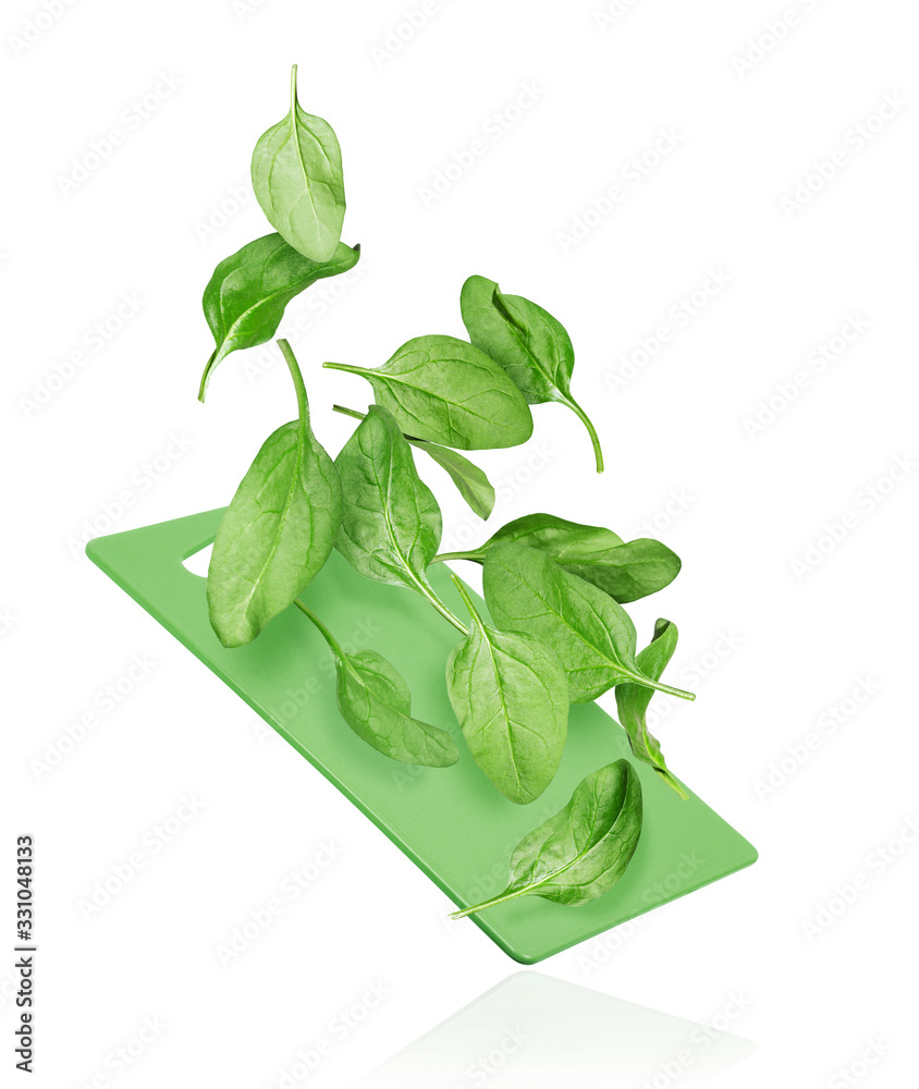 Spinach leaves fall on a kitchen board on a white background