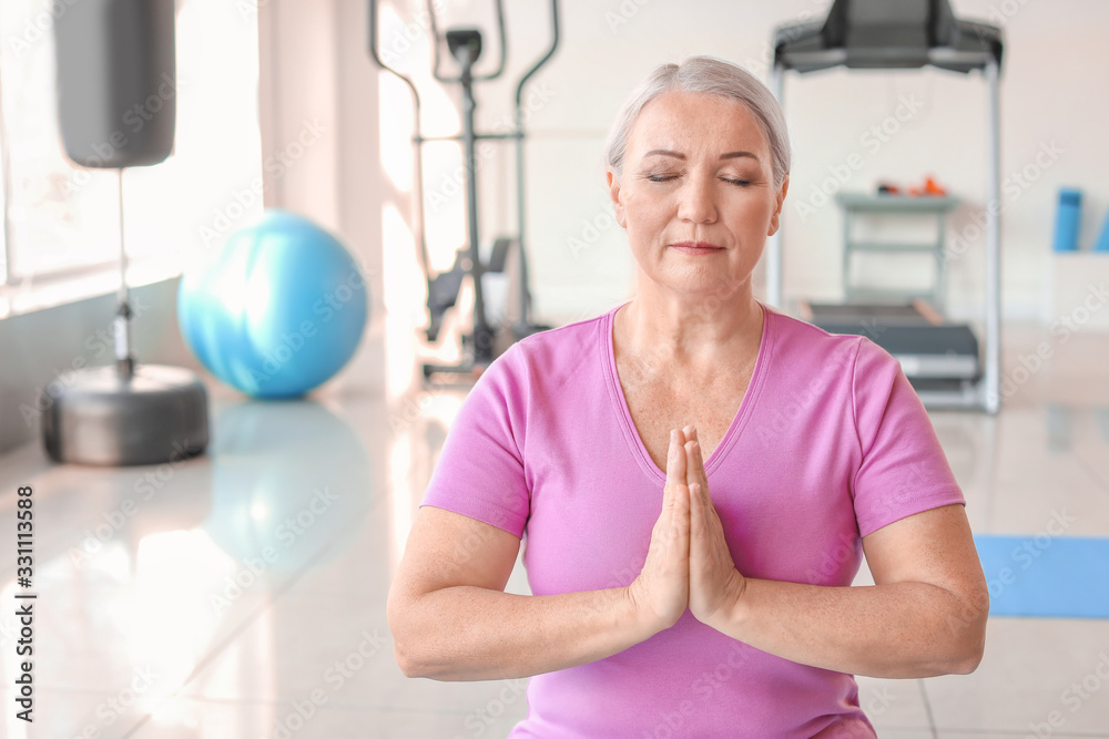 Sporty mature woman practicing yoga in gym