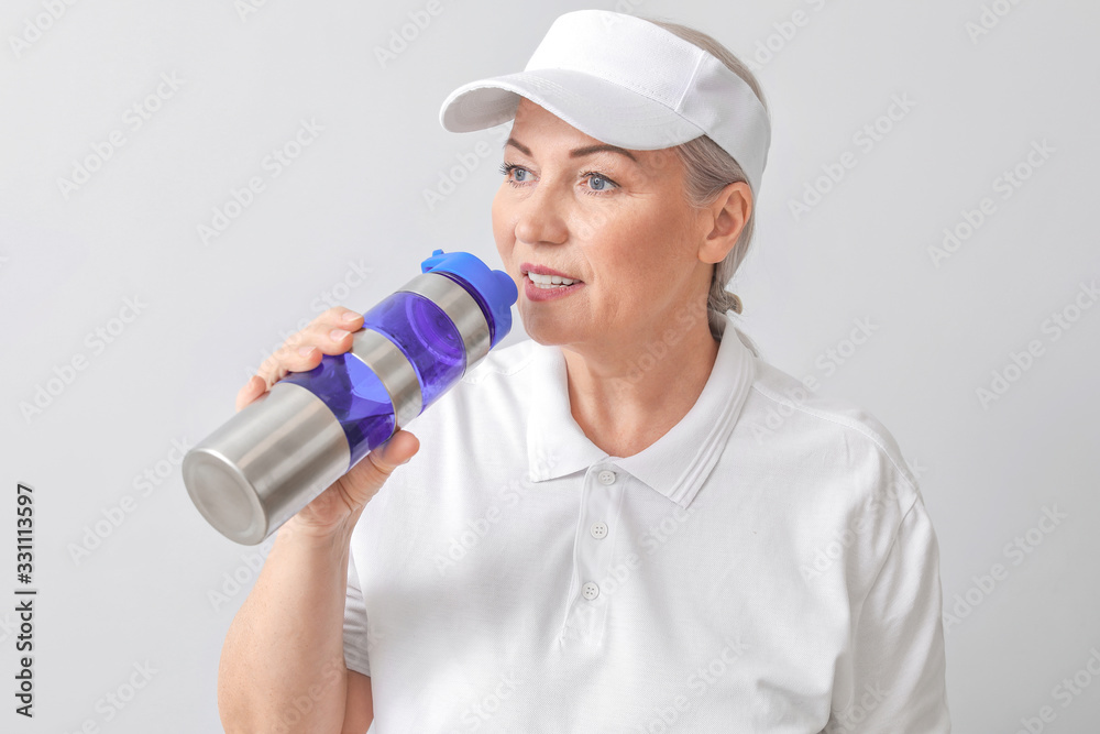 Sporty mature woman with bottle of water on light background