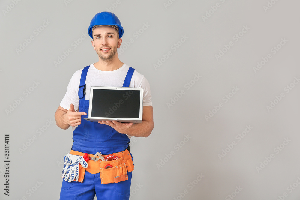 Handsome male worker with laptop on grey background