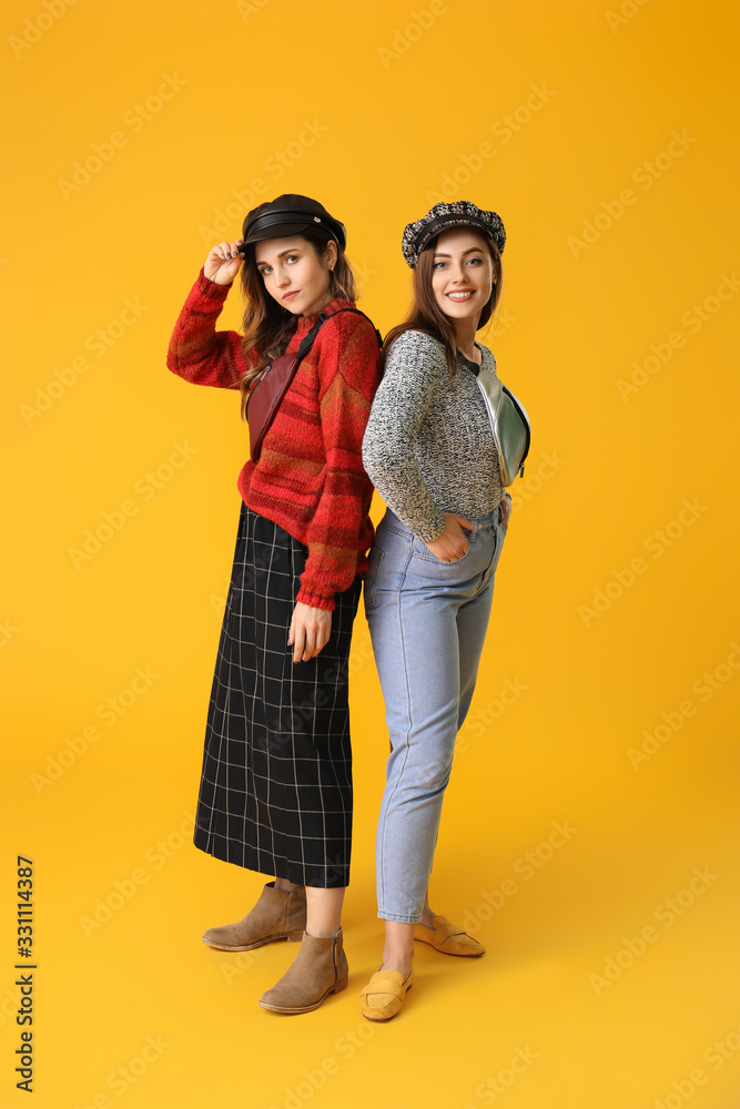 Young women in warm sweaters on color background