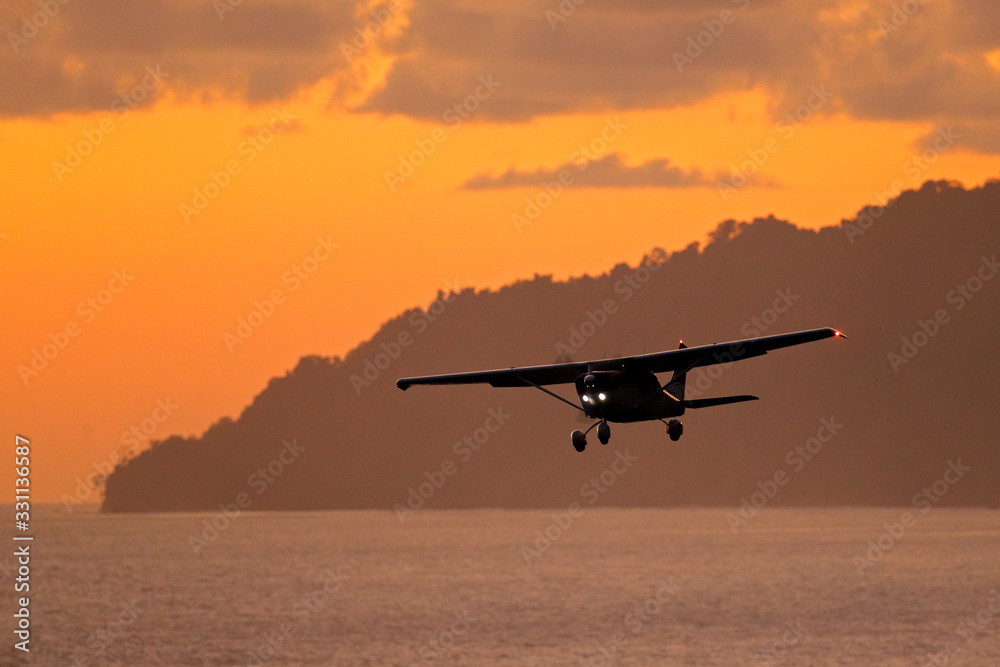 Aircraft on the orange sky with dark clouds. Airplane in the wil nature. Forest hill near the ocean 