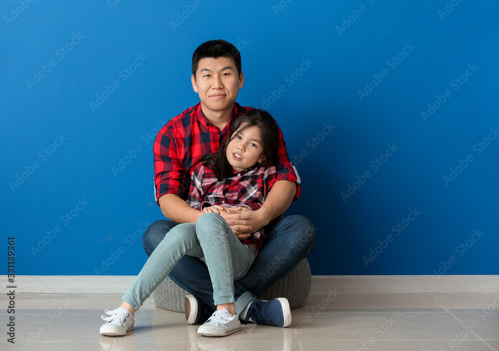 Happy Asian man and his little daughter near color wall