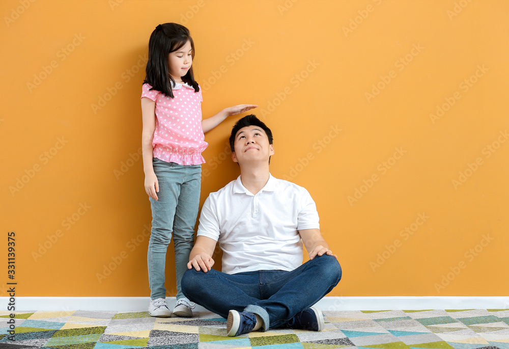 Asian girl measuring height of her father near color wall