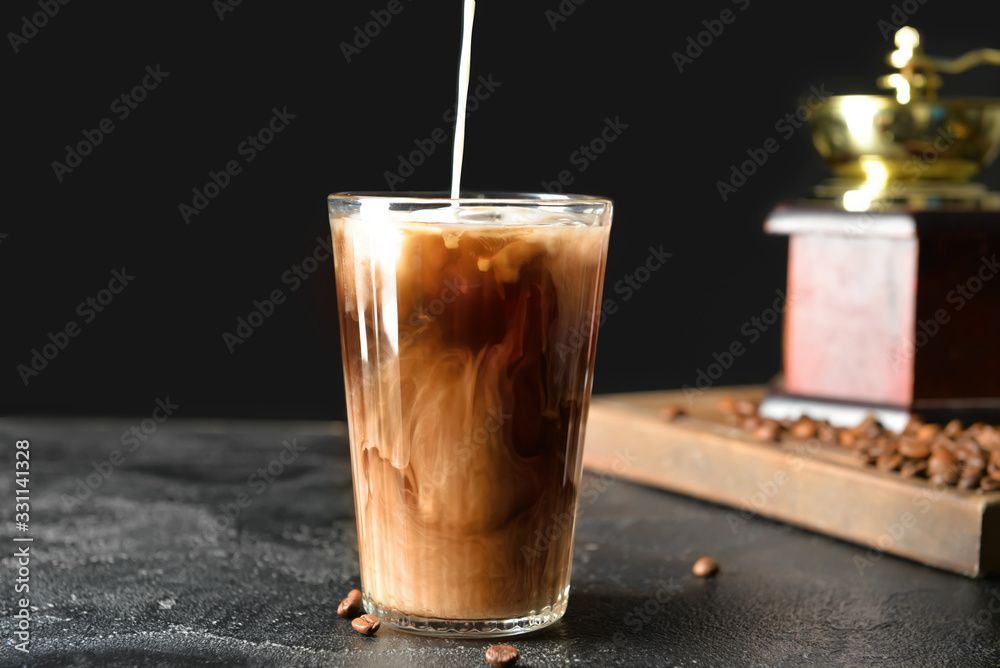 Pouring of milk into cold coffee in glass on table