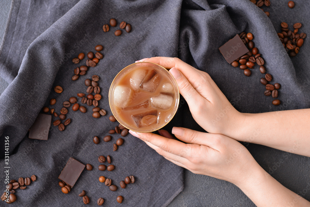 Female hands with glass of tasty iced coffee on dark background