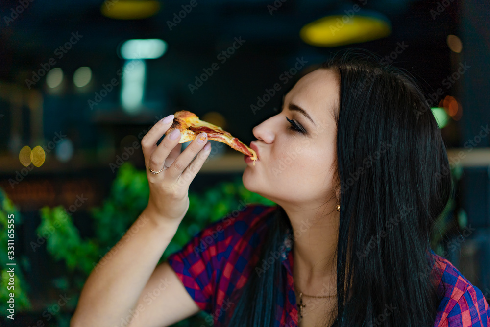 Beautiful brunette girl in t-shirt eating pizza at restaurant. A pretty girl feels happy and enjoys 