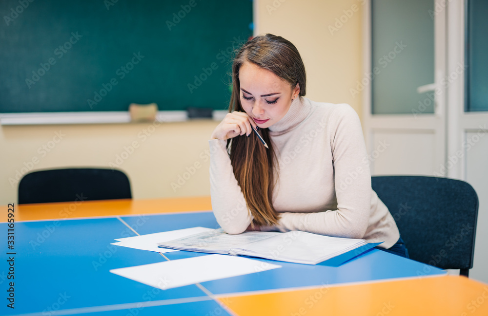 Beautiful young teacher checking notes. Woman teacher in classroom. Blackboard background.