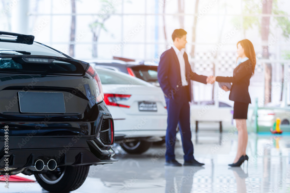 Selective focus on a new car and blur the dealership professional salesman and his client shaking ha