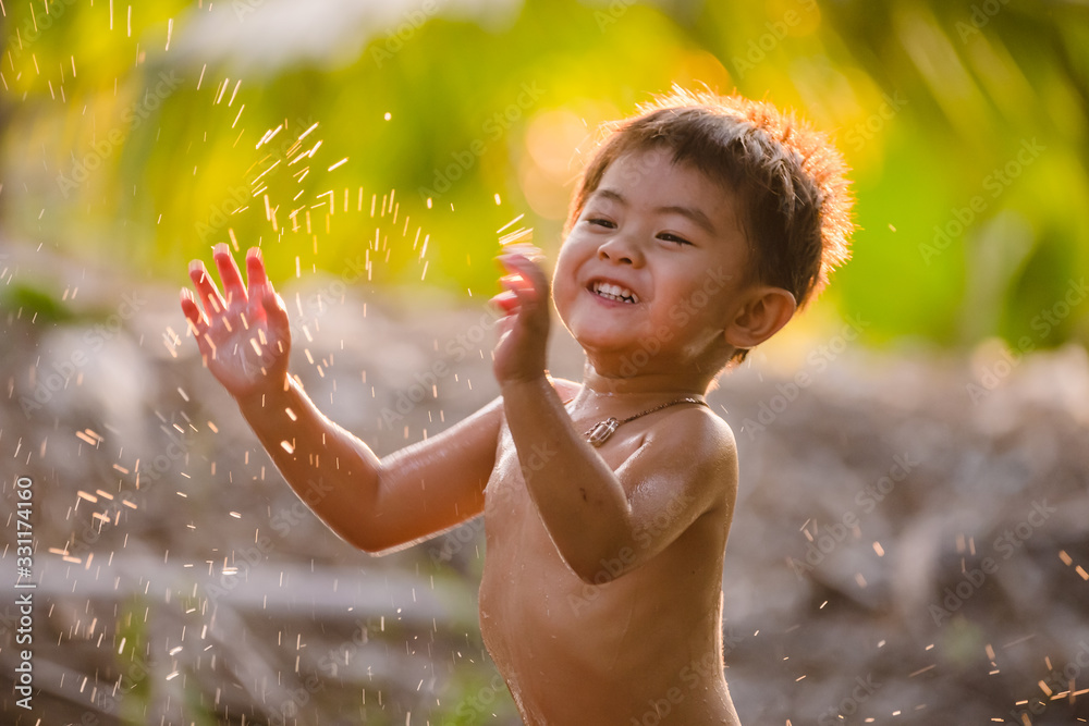 Asia boy smiling and playing with splashes water drops.