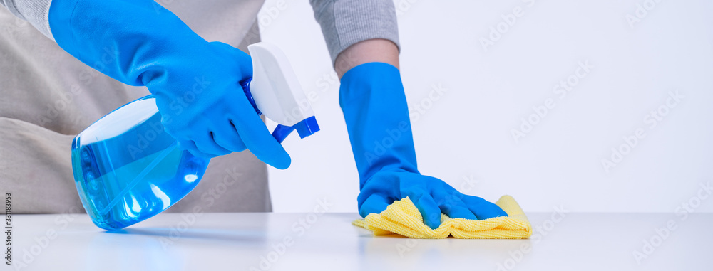 Young woman housekeeper in apron is cleaning, wiping down table surface with blue gloves, wet yellow