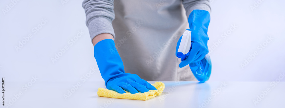 Young woman housekeeper in apron is cleaning, wiping down table surface with blue gloves, wet yellow